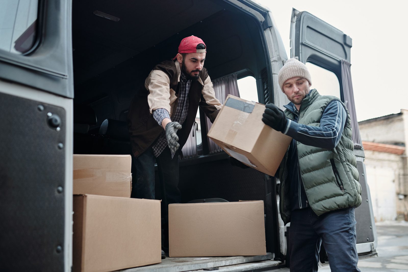 Two men unload cardboard boxes from the back of a van.