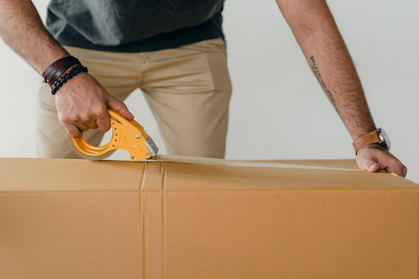 Hands sealing a cardboard box with a tape gun.