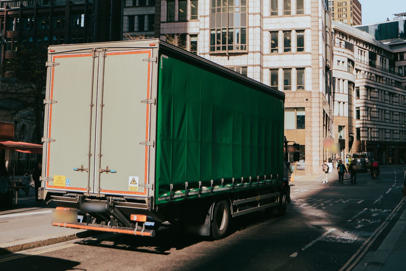 A curtain-sided lorry on a London street between office blocks.